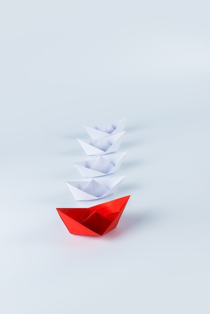 Red paper ship leading among white