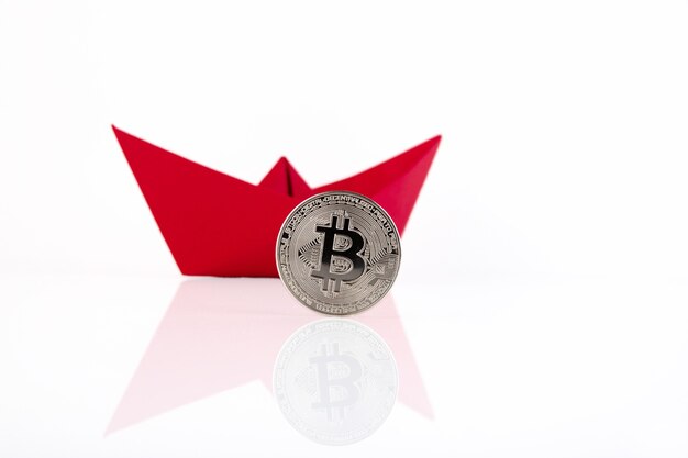 Red paper ship, platinum bitcoin coin on white