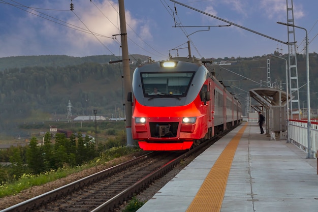 Un treno passeggeri rosso arriva alla stazione ferroviaria. comunicazione interurbana.