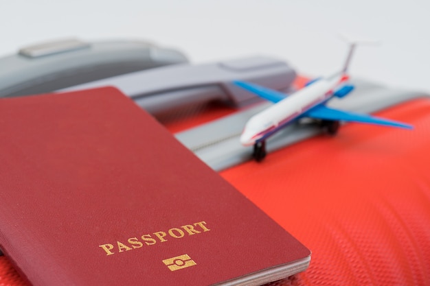 The red passport and model of the plane lie on the red suitcase.