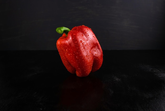 Red pepper in water drops closeup on a dark wooden background