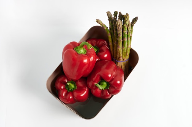 Red peppers and asparagus in a plastic container on a white background