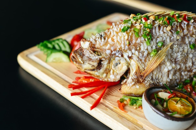 Red perch grilled in batter with vegetables and greens on wooden chop board isolated on black backgr