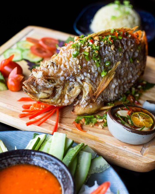 Red perch grilled in batter with vegetables and greens on wooden chop board isolated on black backgr