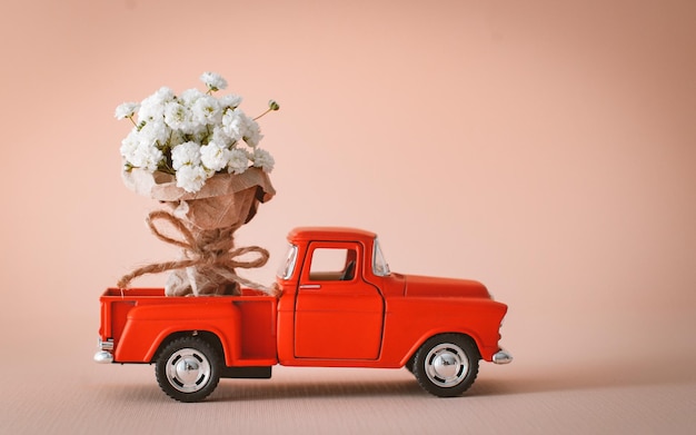 Red pickup retro toy car delivering bouquet of flowers. February 14 card, Valentine's day. Flower delivery. 8 March, International Happy Women's Day.