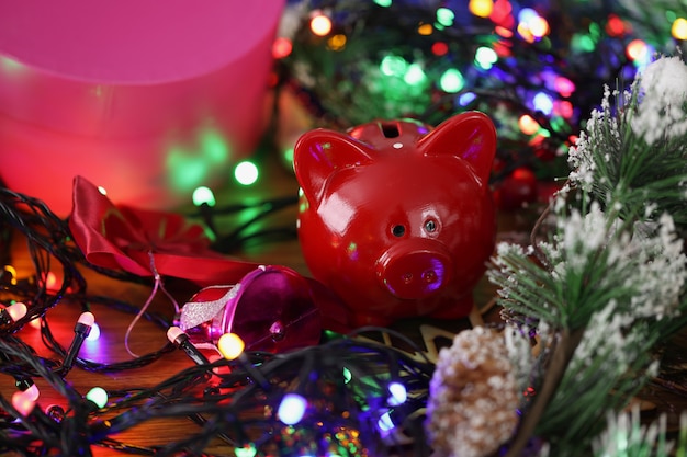 Photo red piggy bank standing among bright shiny new year garland closeup. saving for christmas concept