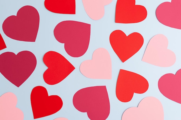 Red and pink paper hearts of various size lying on pastel blue background
