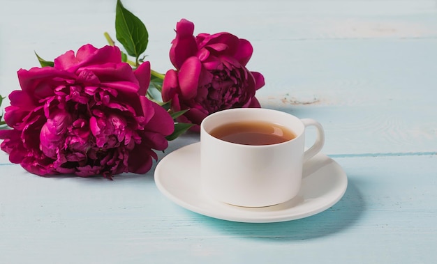 Red pink peonies tea cup on a blue wooden background Horizontal frame copy space for text design