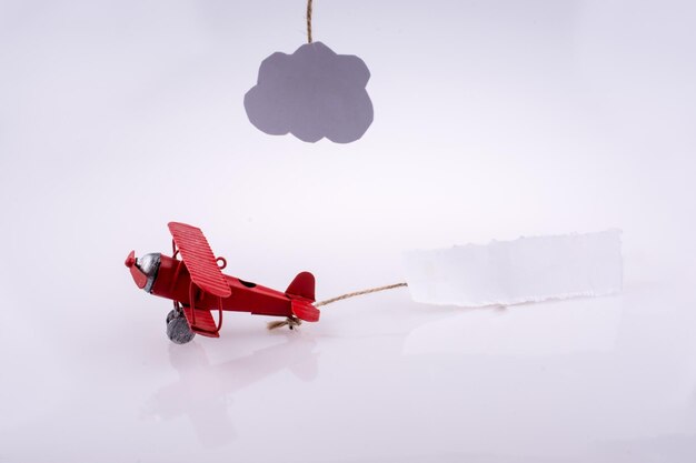 A red plane is pulling a string with a cloud hanging from it.