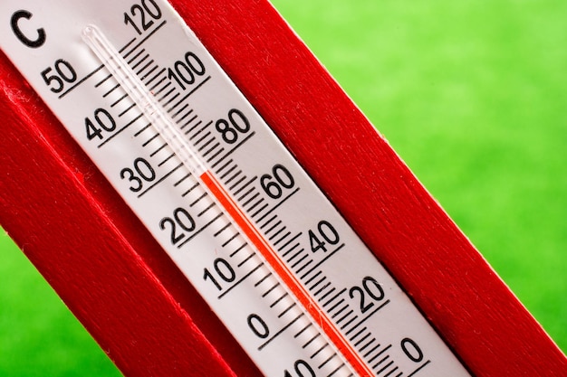 Photo a red plastic thermometer on a green background