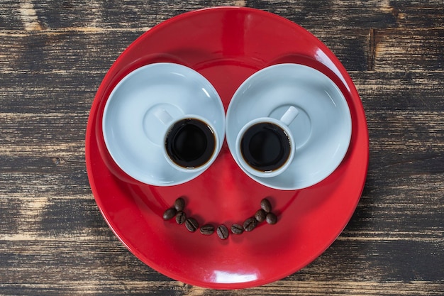 Piatto rosso insieme a due tazze di caffè e un sorriso dai chicchi di caffè su un tavolo di legno primo piano vista dall'alto