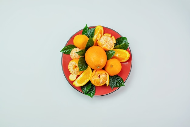 Photo red plate of oranges and tangerines with green leaves on a light background