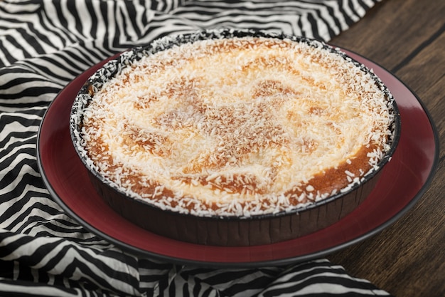 Red plate of sweet pie with coconut sprinkles on wooden surface