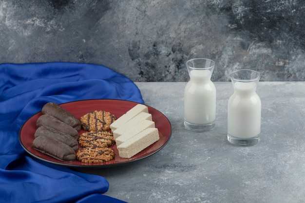 A red plate with oatmeal cookies and chocolate sticks with glass of milk.