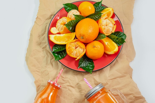 Red plate with oranges and tangerines green leaves bottle with juice on light background Top view copy space