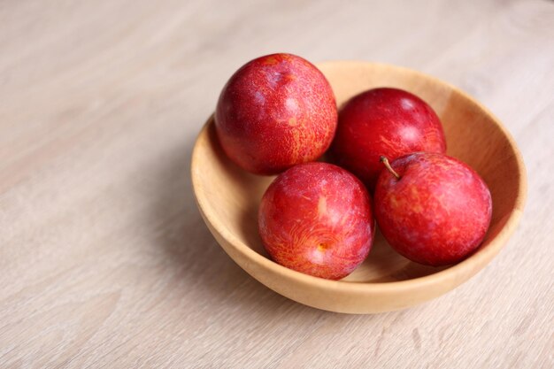 Photo red plum in wooden bowl on wooden background