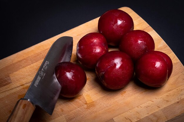 Prugne rosse su tagliere di pane con coltello e sfondo nero