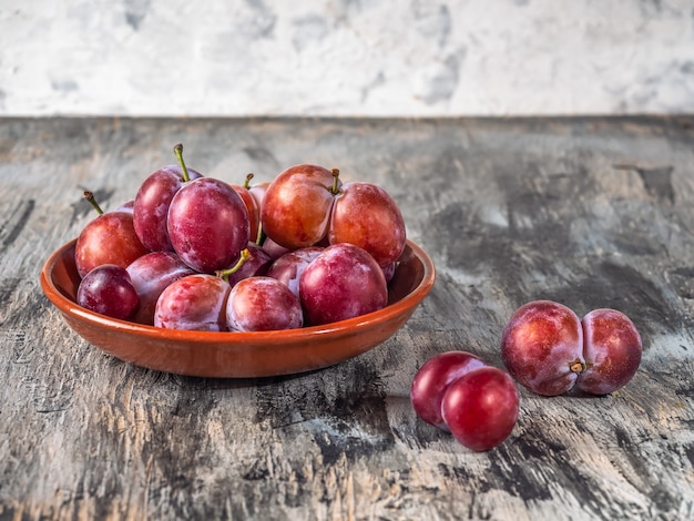 Red plums, twin fruit on a clay plate close-up on a gray background