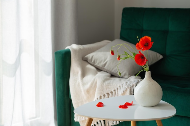 Red poppies in vase in modern cozy interior with green coach