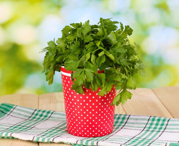 Red pot with parsley and dill on wooden table on natural background