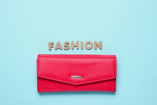 Red purse on blue surface with text fashion with letters.