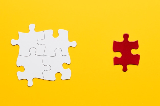 Photo red puzzle piece standing separately from white puzzle piece on yellow backdrop