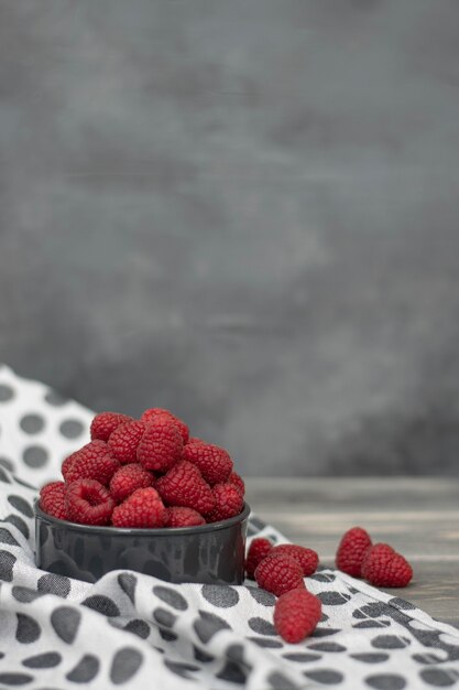 Red raspberries in bowl on grey wooden background. Fresh berries.