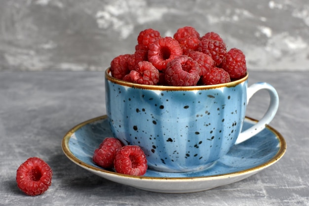 Red raspberries closeup in a blue cup on a gray background