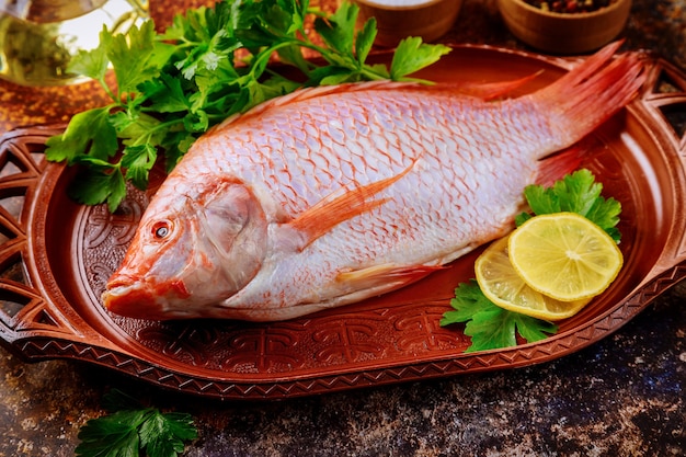 Red raw tilapia fish with herbs, lemon olive oil