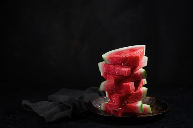 Red raw watermelon pieces on dark background with copy space. It sweet, juicy flesh, usually deep red to pink, with many black seeds, although seedless varieties exist