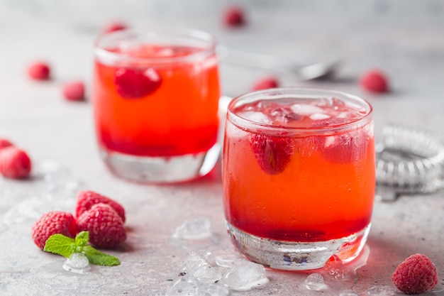 Красный освежающий холодный малиновый лимонад в стаканах со льдом и ягодами
