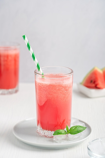 red refreshing cold watermelon juice served in drinking glass with ice cubes and paper straw