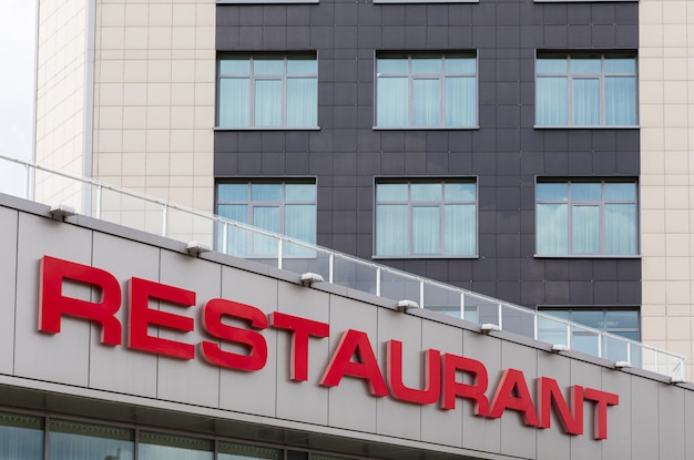 Фото Красное название ресторана на современный серый кафельный фасад здания.