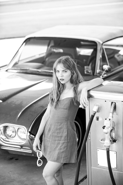 赤いレトロな自動車古いアメリカの自動車ガソリンスタンドの女の子の女性は自動車に燃料を補給します