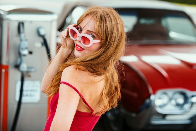 赤いレトロな自動車オールドアメリカンカーガソリンスタンドで笑顔の女性