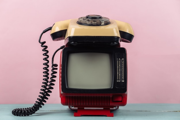 Red retro old portable mini tv set with rotary telephone on pink background.