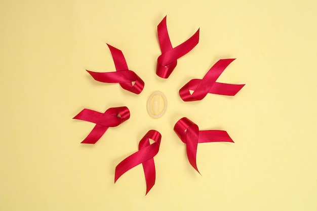 Red ribbon and condom symbol against HIV isolated on yellow background