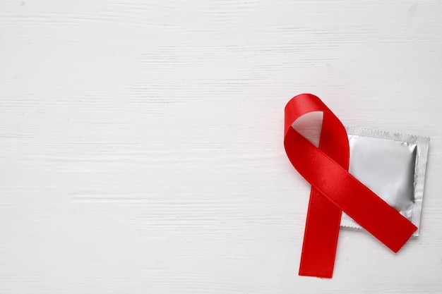 Photo red ribbon and condom on white wooden background flat lay with space for text aids disease awareness