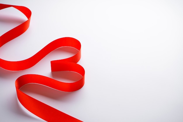 Red ribbon in the form of a heart on a white background with place for text.