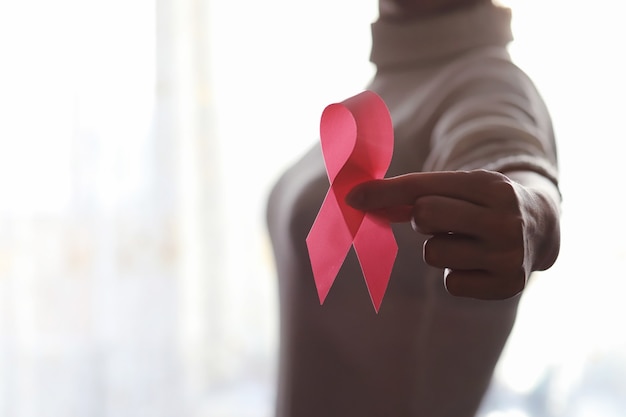 The red ribbon of the girl. The girl is holding a red ribbon. Health concept red ribbon. Breast cancer.