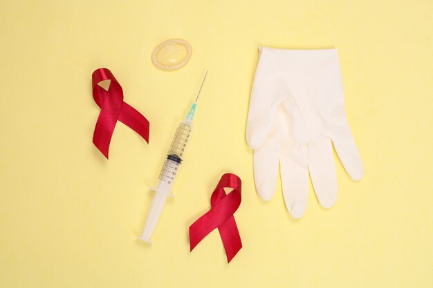 Nastro rosso e simbolo del dispositivo medico contro l'hiv isolato su sfondo giallo