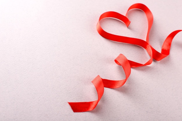 Red ribbon in shape of heart on light textured background