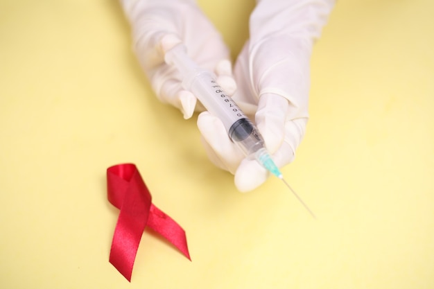 Nastro rosso con guanti medici e siringa contro l'hiv isolato su sfondo giallo Foto Premium