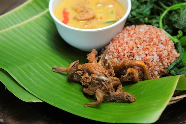 Red rice with salted fish spinach chilli sauce and sayur lodeh on banana leaf Indonesian food