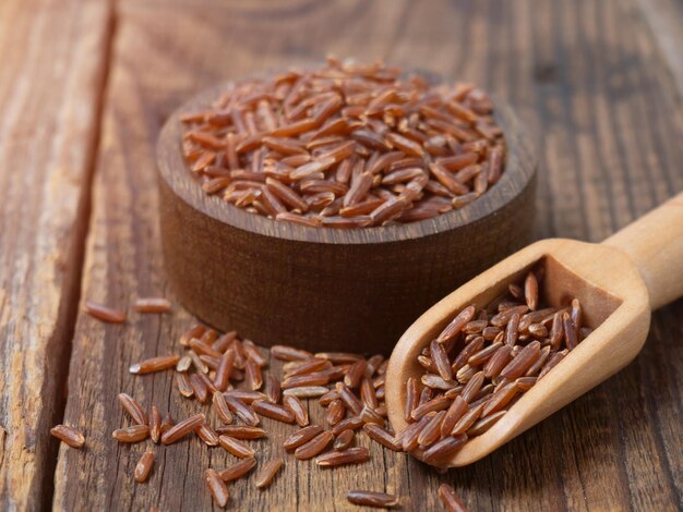 Red rice in a wooden scoop on a dark wooden rustic\
background