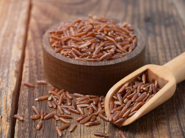 Red rice in a wooden scoop on a dark wooden rustic background