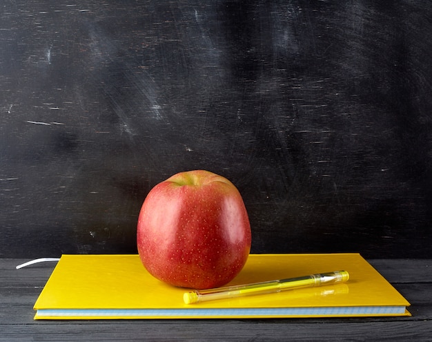 Photo red ripe apple lies on a yellow closed notebook