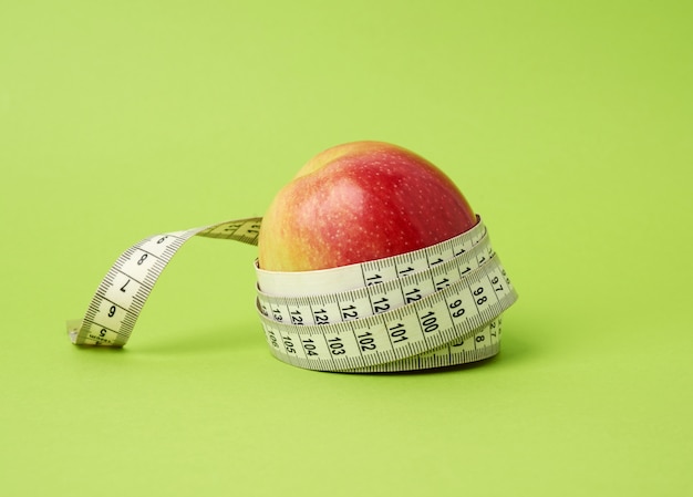 Красное спелое яблоко, завернутое в сантиметр на зеленом фоне, концепция контроля веса тела, потеря веса
