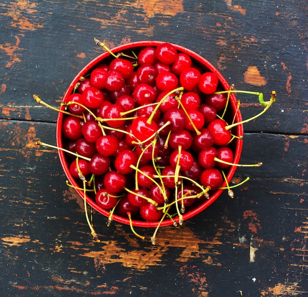 Red ripe cherries with tails in a round platet on the old black wood background with crack. close-up top view