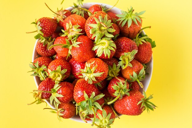 Red ripe juicy strawberry in a plate on yellow